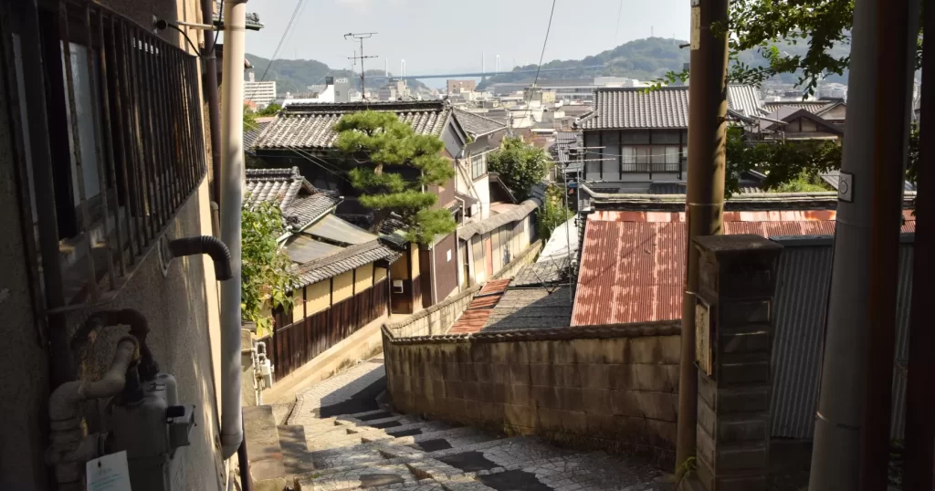 石段の坂道から見下ろす瓦屋根の家並みと、奥に見える尾道水道と橋